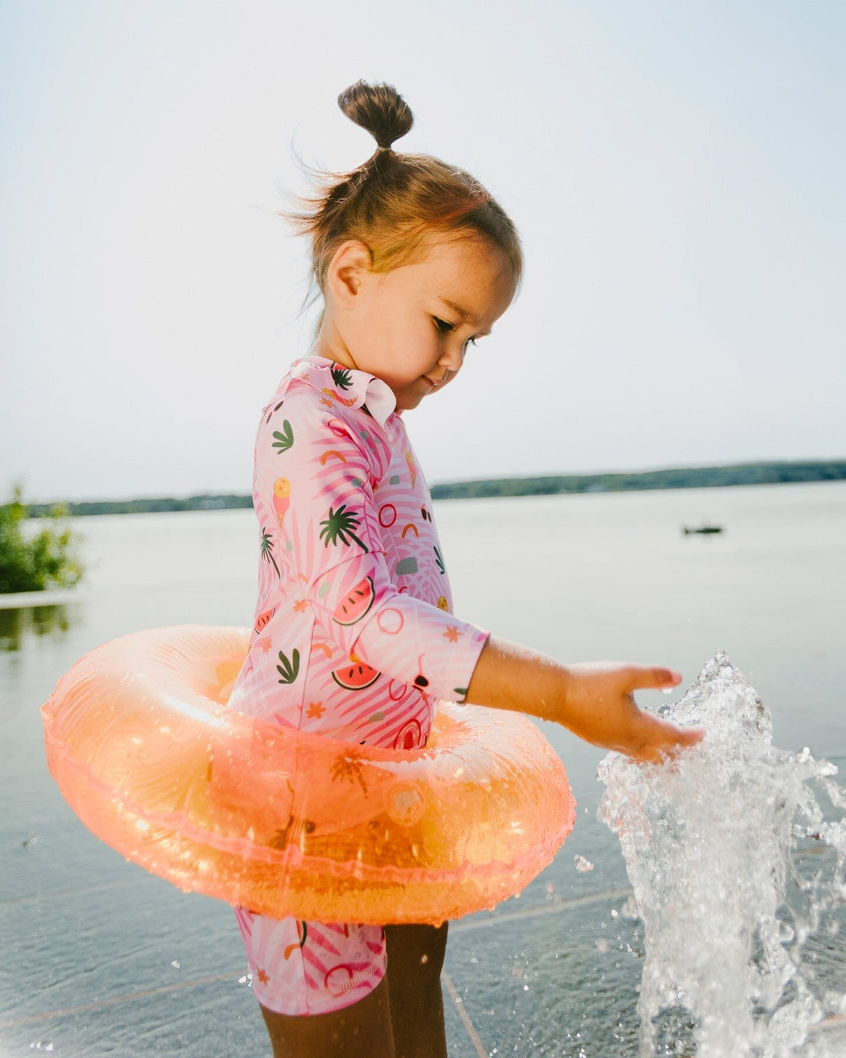 Back view of toddler girl in pink long sleeve rashguard swimsuit with beach print