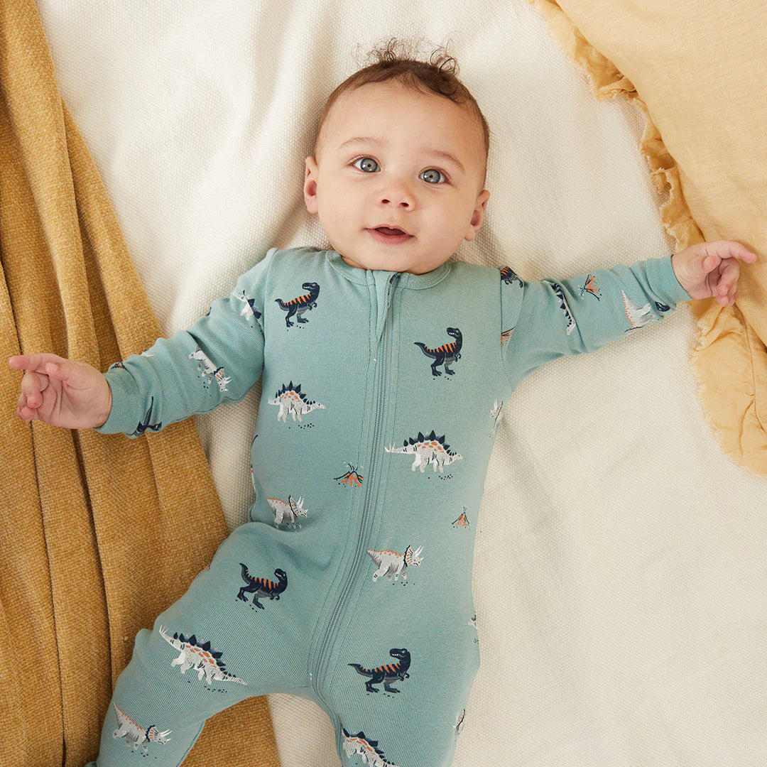 Infant wearing tidal wave green dinosaur print footed sleeper with two-way zipper