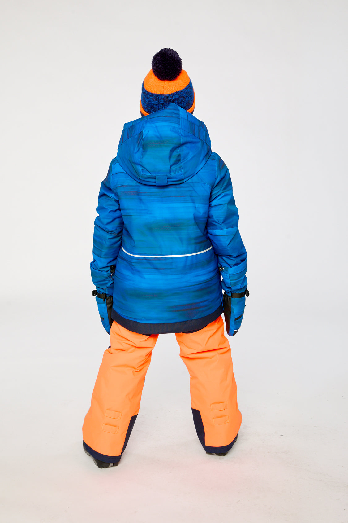 Back view of a boy wearing the blue jacket and orange snow pants