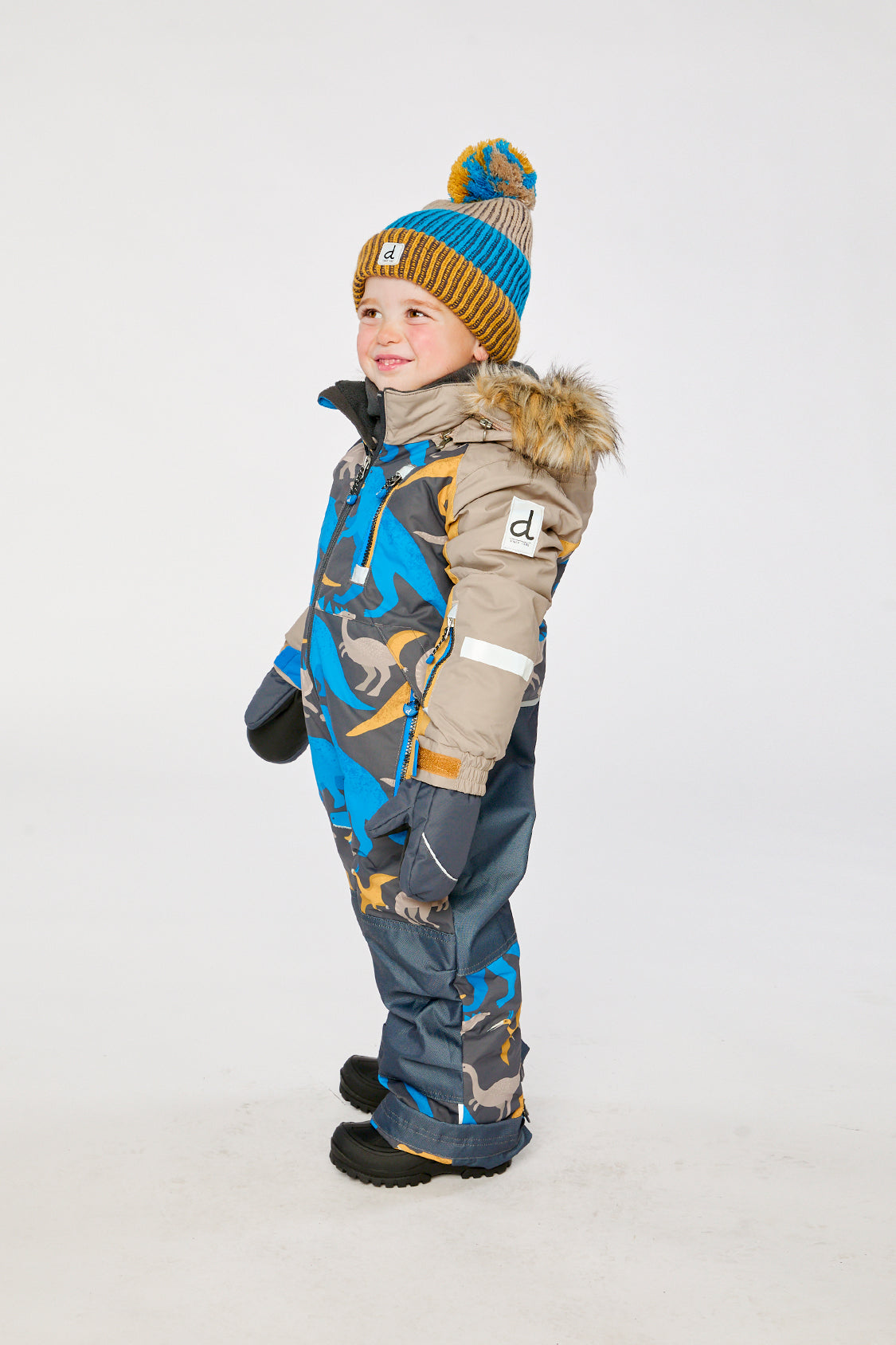 Child wearing the Deux par Deux grey and blue dinosaur PLAY one-piece snowsuit, side view