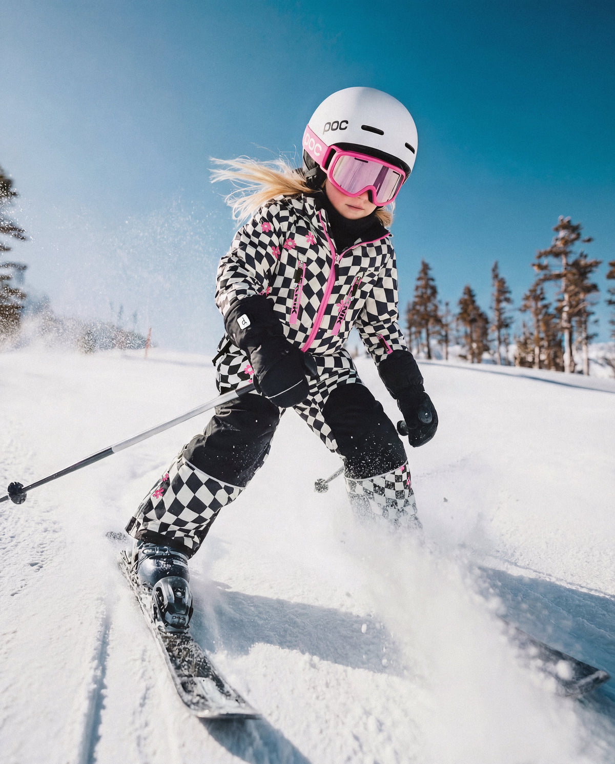 Girl skiing downhill in the checkered Deux par Deux TEKNIK snowsuit and a white helmet
