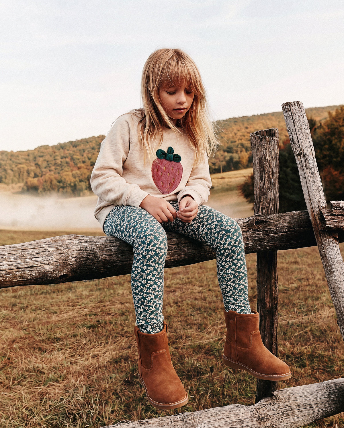 Child wearing the Deux par Deux teal daisy print leggings with brown boots on a wooden fence outdoors