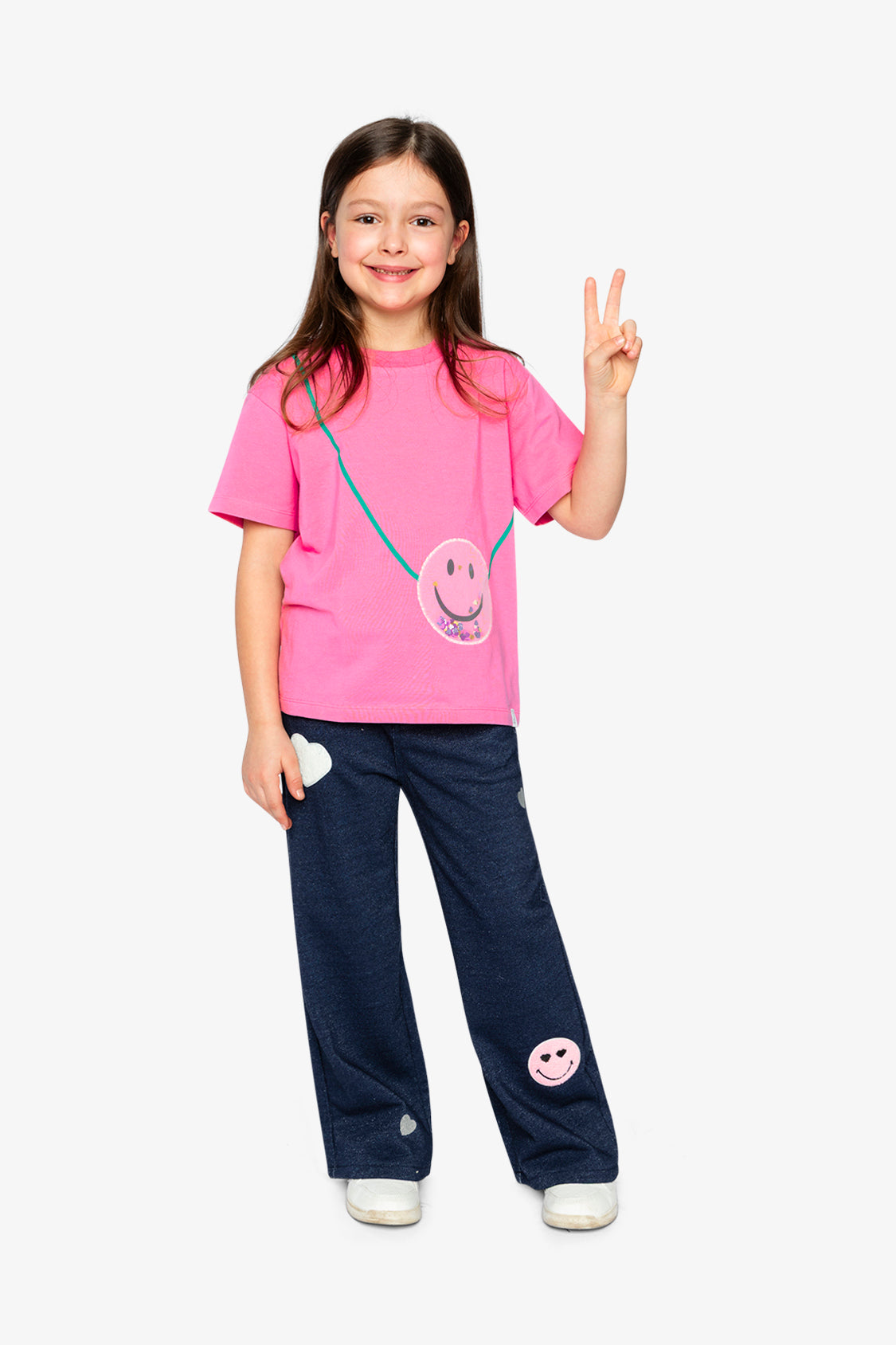 Full-length look of the pink smiley top with navy wide-leg pants and white sneakers