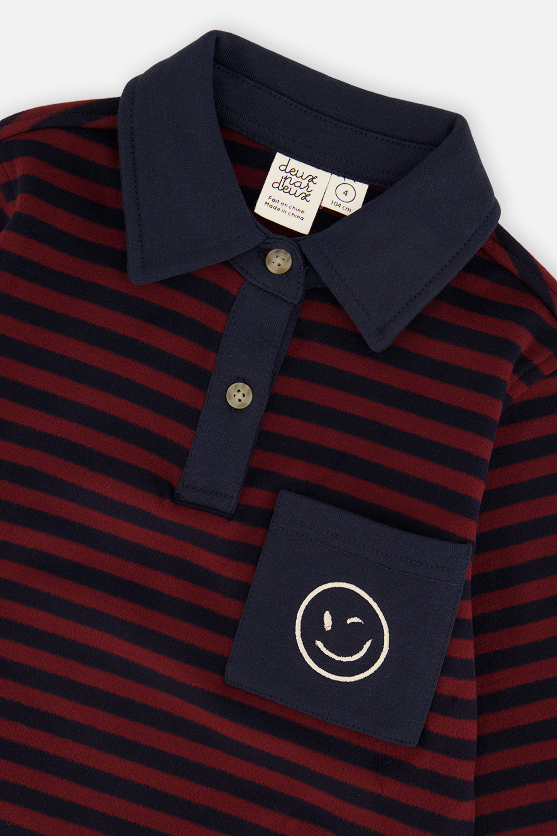 Close-up of the navy polo collar, two buttons and smiley pocket on the striped top