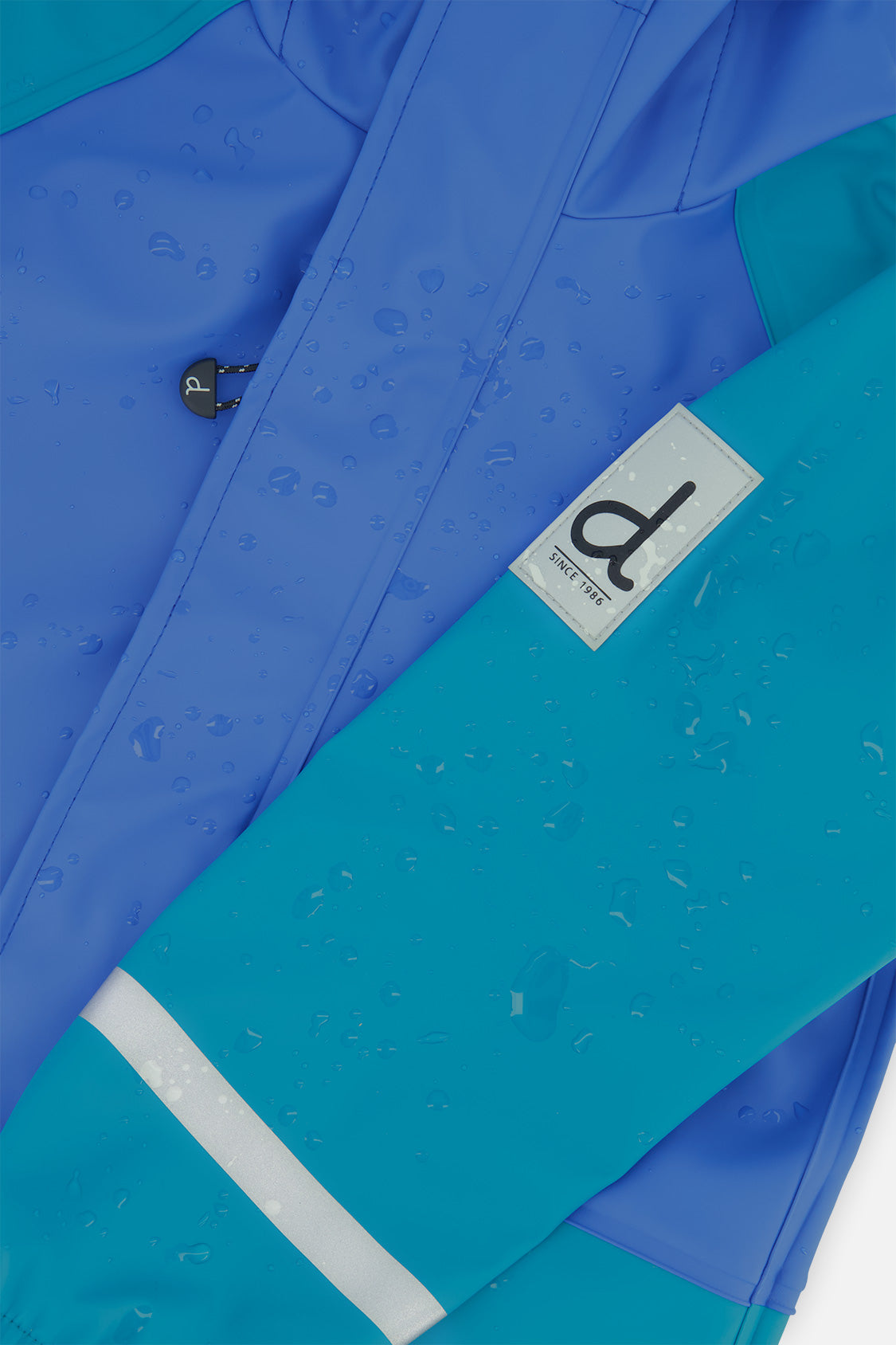 Close-up of the Deux par Deux label and reflective band on the dark turquoise rain jacket sleeve
