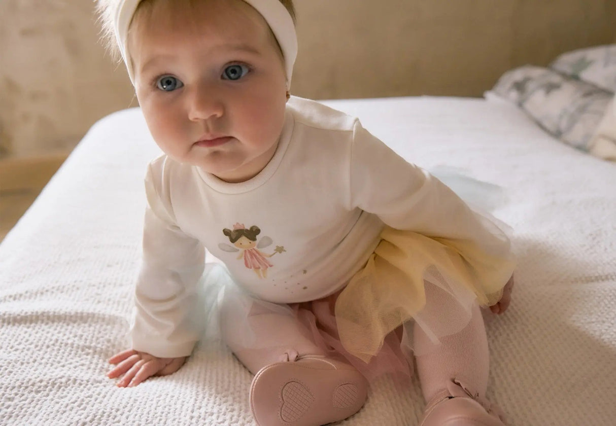 Baby girl wearing bodysuit and skirted tights, closeup of elastic cuffs and soft cotton for gentle comfort.