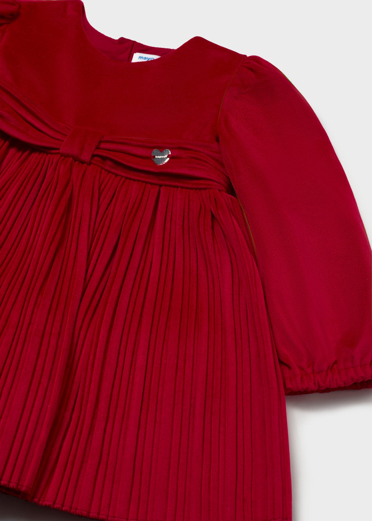 Close-up of the bow and small heart charm on the red pleated dress