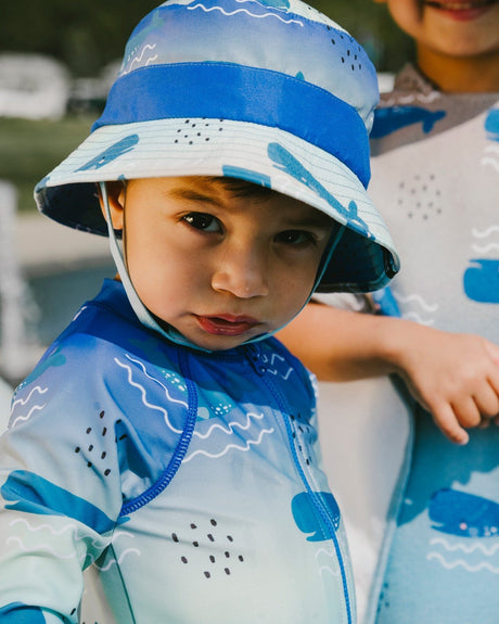 Close-up of baby boy wearing blue whale rashguard one-piece and matching sun hat