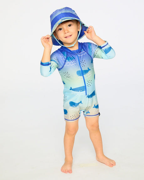 Toddler boy standing in blue whale long sleeve rashguard swimsuit front view