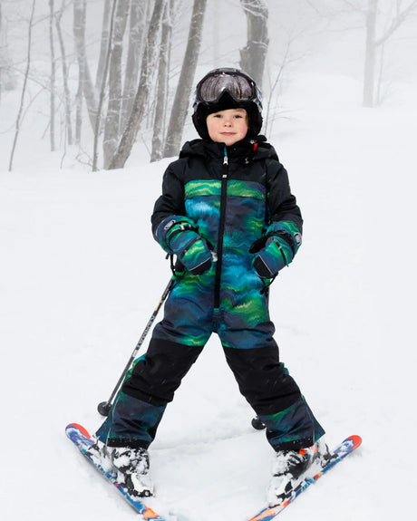 Child wearing Aurora Borealis one-piece Teknik snowsuit – front on snow