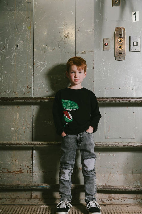 Cool boy in black dinosaur graphic sweatshirt and grey jeans – trendy casual kidswear outfit from Jenni Kidz USA & Canada.