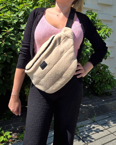Adult wearing a cream sherpa version of the Deux par Deux changing sling bag across the chest
