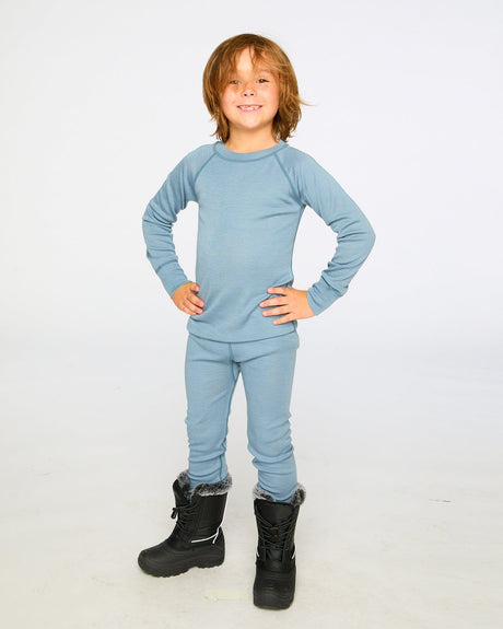 Smiling child in the blue gray merino wool base layer set and black snow boots