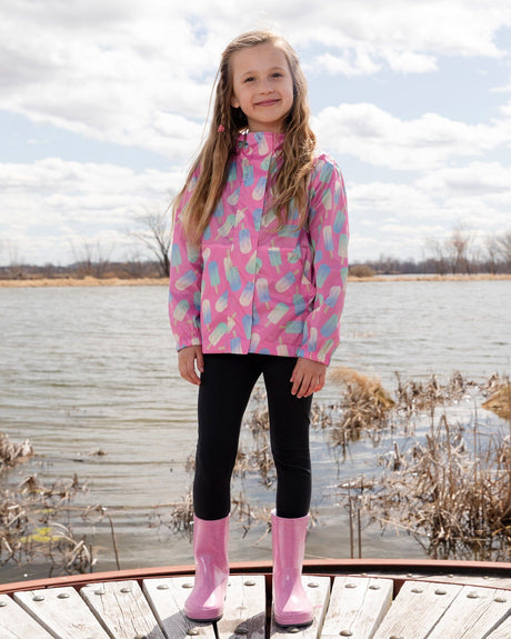 Child by a lake wearing the pink lollipop windbreaker with black leggings and pink boots