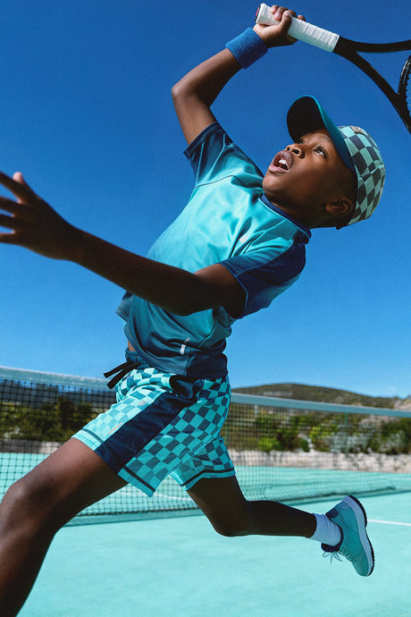 Child playing tennis in the teal checkerboard shorts and a teal top