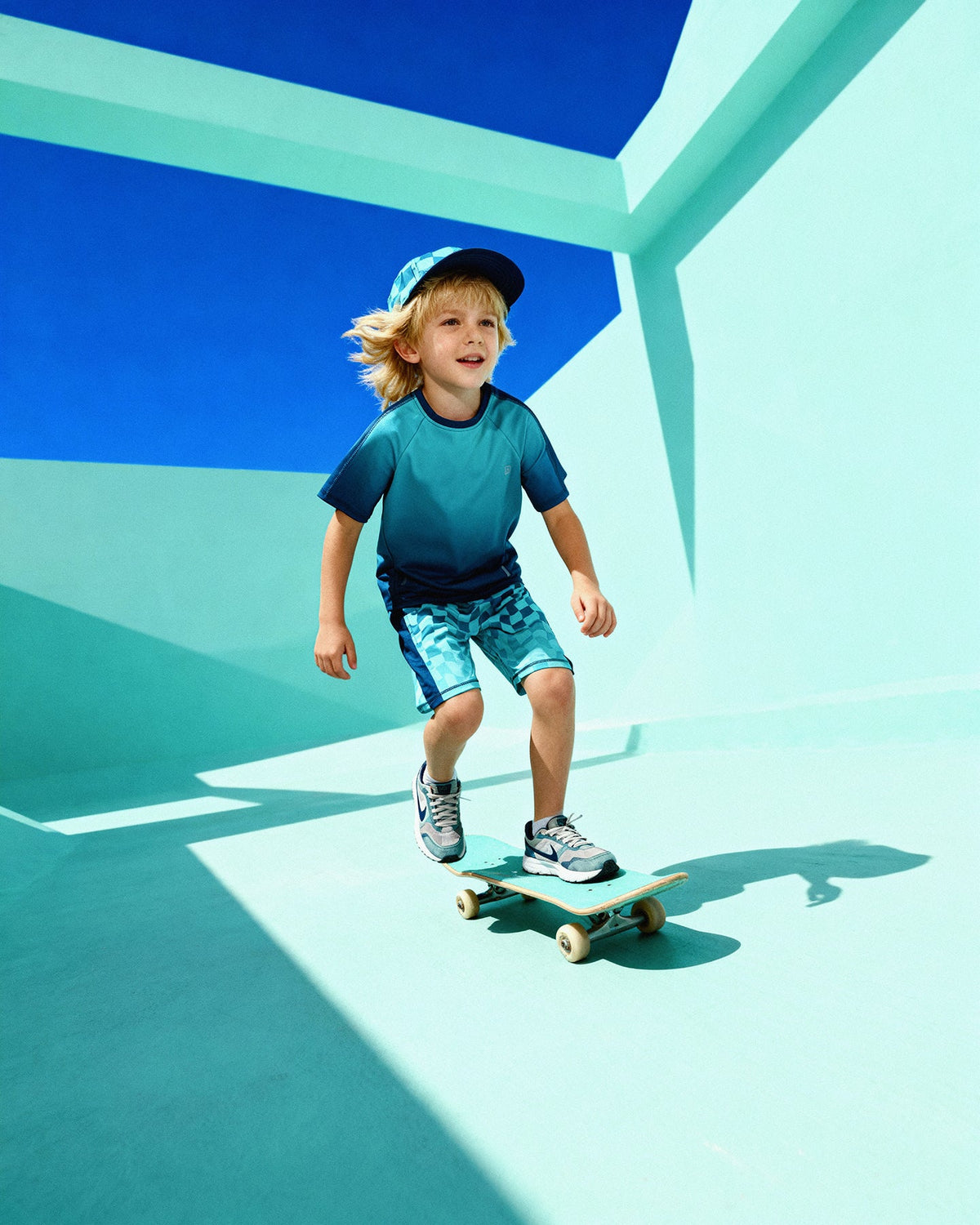 Child skateboarding in the teal gradient athletic top with printed shorts and cap