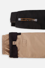 Close-up of the black PLAY jacket ski-pass sleeve pocket and the adjustable beige pant hem
