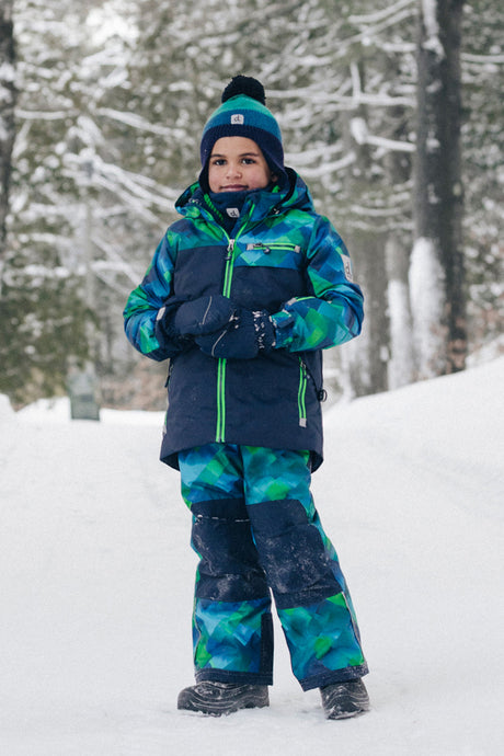 Child wearing the Deux par Deux blue and green checkered PLAY snowsuit on a snowy trail