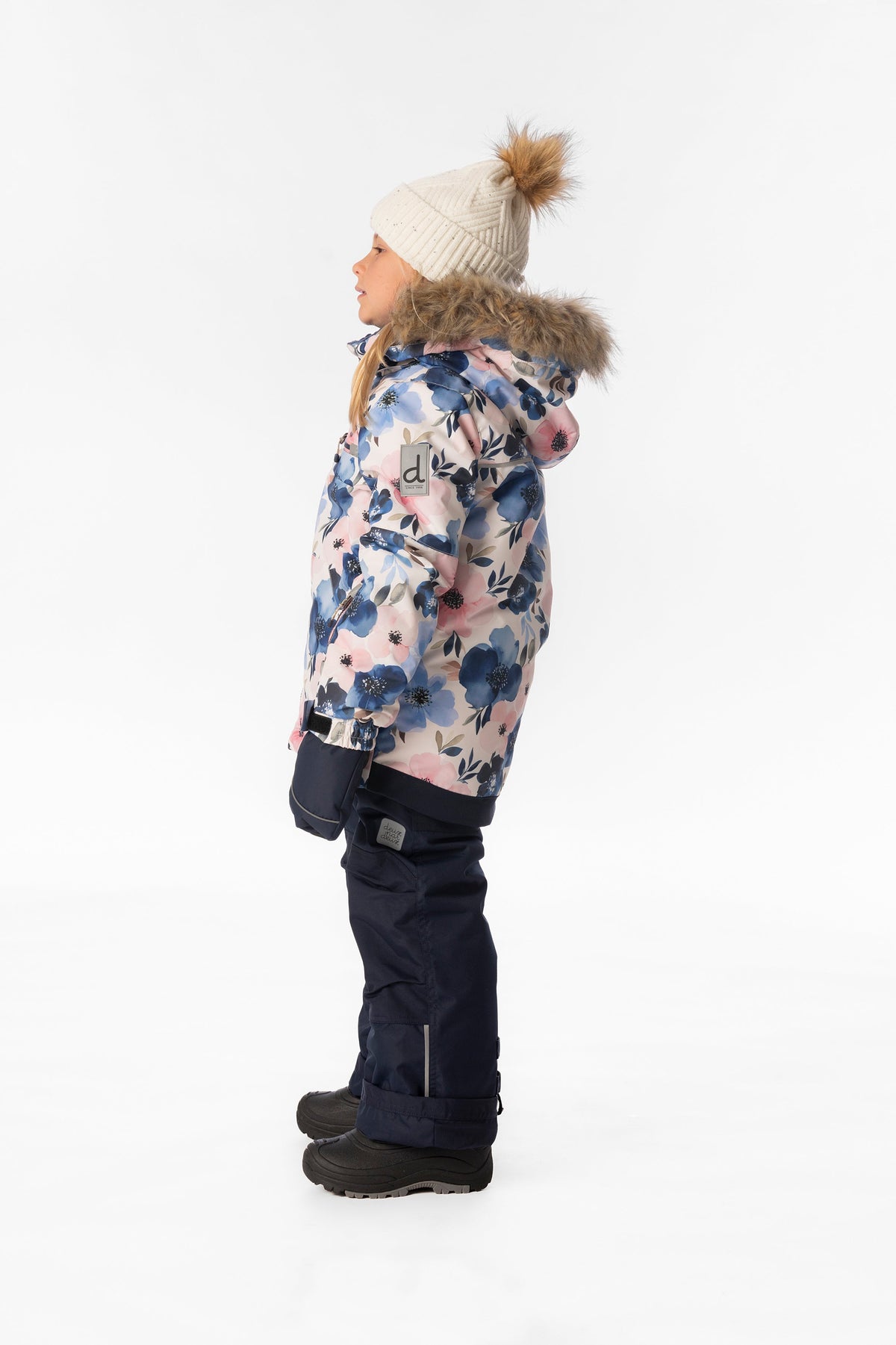 Side view of a girl wearing the watercolor flower PLAY jacket and navy snow pants