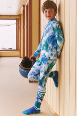 Child leaning against a wall and holding a ski helmet while wearing the blue mountain print thermal set