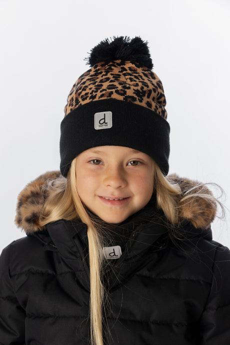 Smiling girl wearing the leopard print knit toque with a black cuff and a black puffer jacket, front view