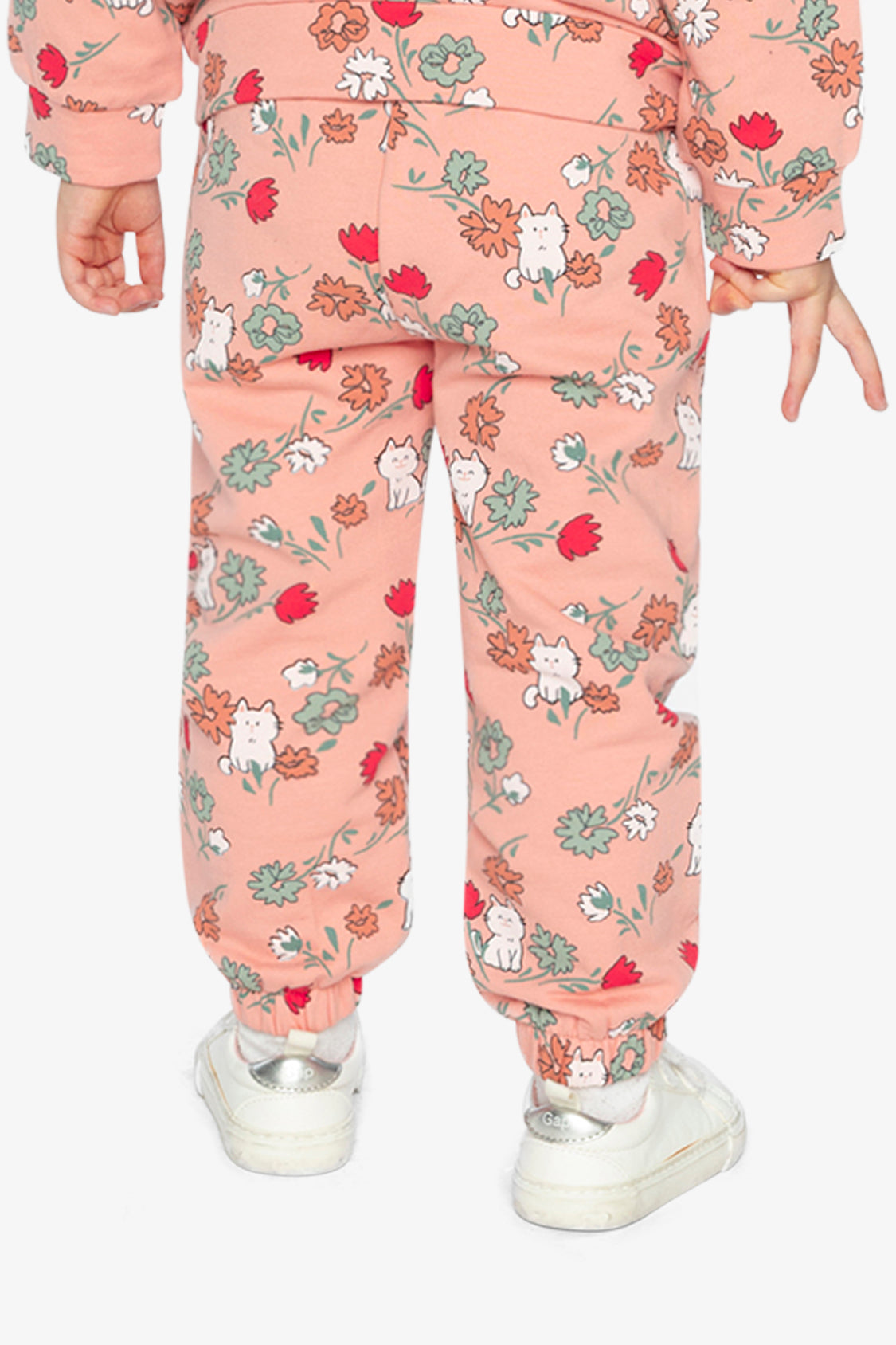 Back view of a child wearing coral pink French terry track pants with a cat print and white sneakers