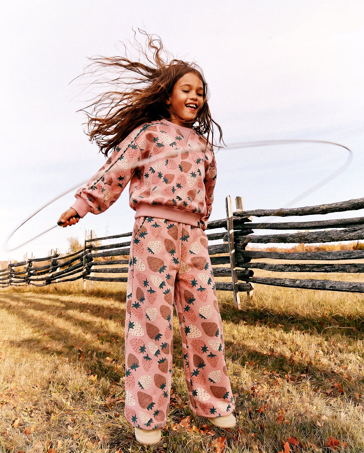 Child spinning a hula hoop outdoors in the strawberry print sweatshirt and matching pants