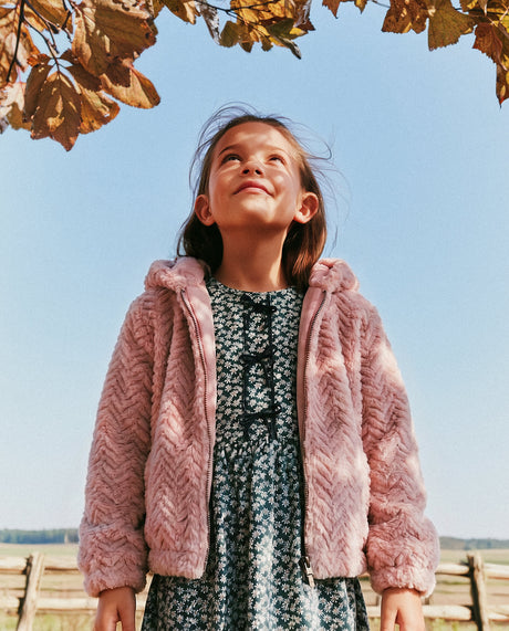 Child wearing the dusty pink faux fur hooded cardigan over a floral dress outdoors