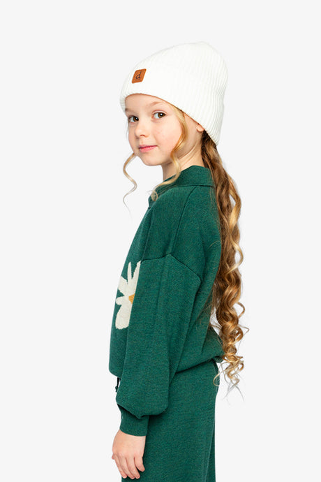 Child wearing the dark green daisy knit sweater and white beanie, side view