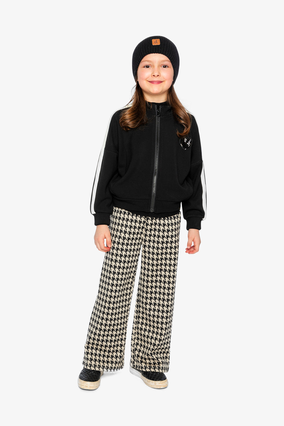 Girl in a black beanie, black jacket with white sleeve stripes and houndstooth flare pants, full-length view