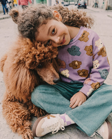 Child wearing the lilac poodle print sweatshirt, sitting next to a large brown poodle on a street