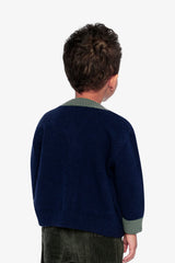 Back view of a child wearing the Deux par Deux navy knit cardigan with green neck trim