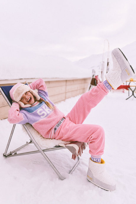 Girl lounging on a deck chair in the snow wearing the light pink base layer leggings