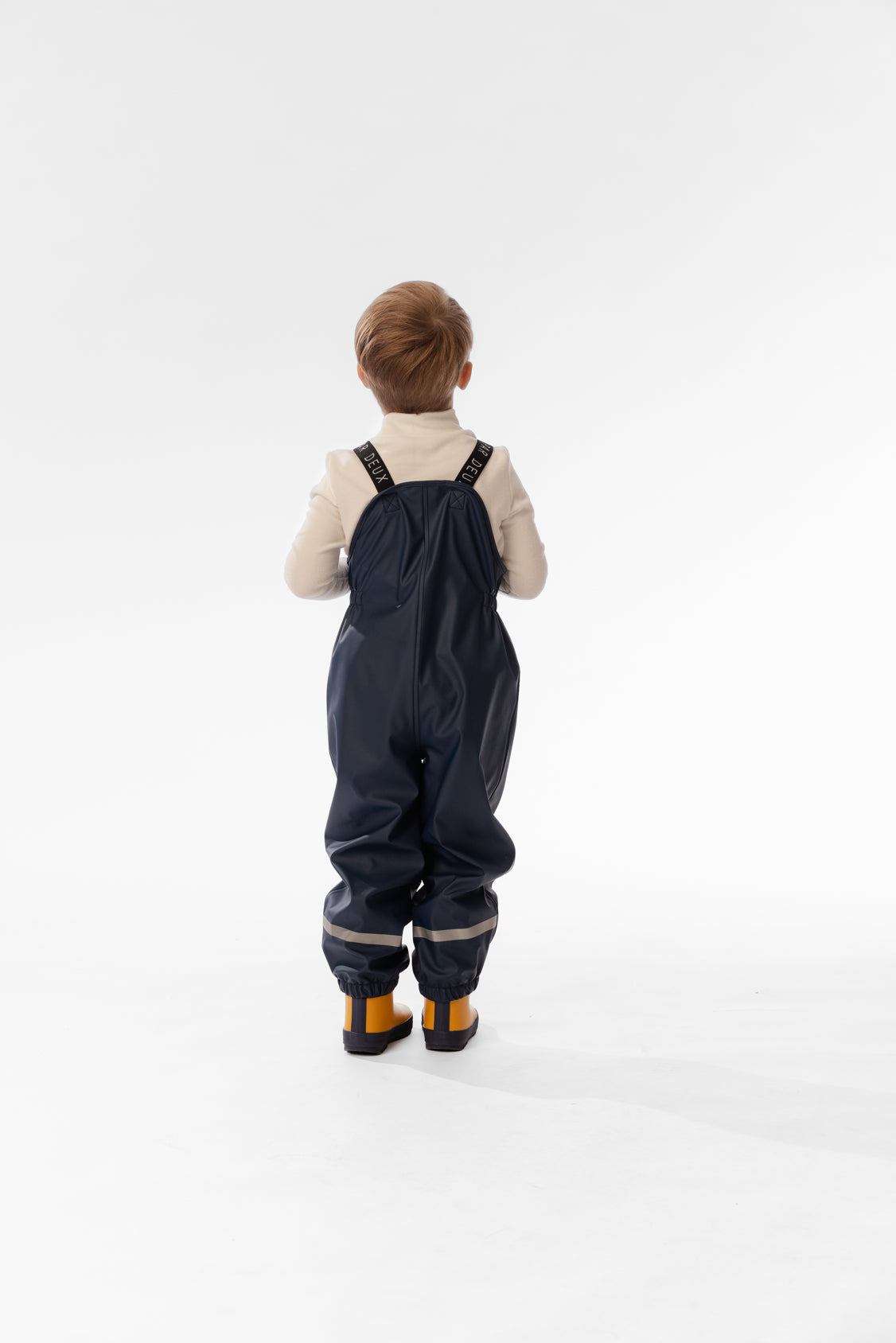 Child wearing the Deux par Deux dark blue rain overalls, back view