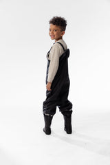 Side view of a child in the Deux par Deux black rain overalls and black rain boots