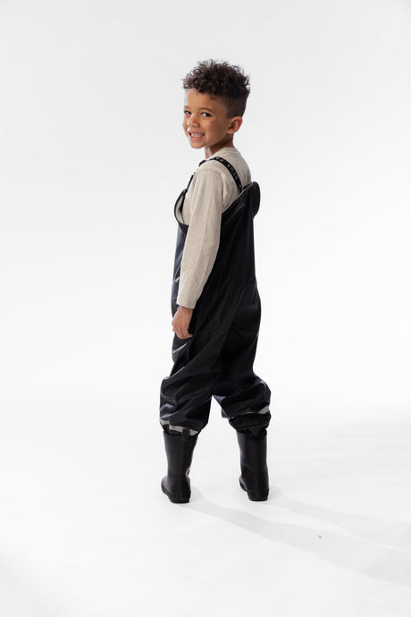 Side view of a child in the Deux par Deux black rain overalls and black rain boots
