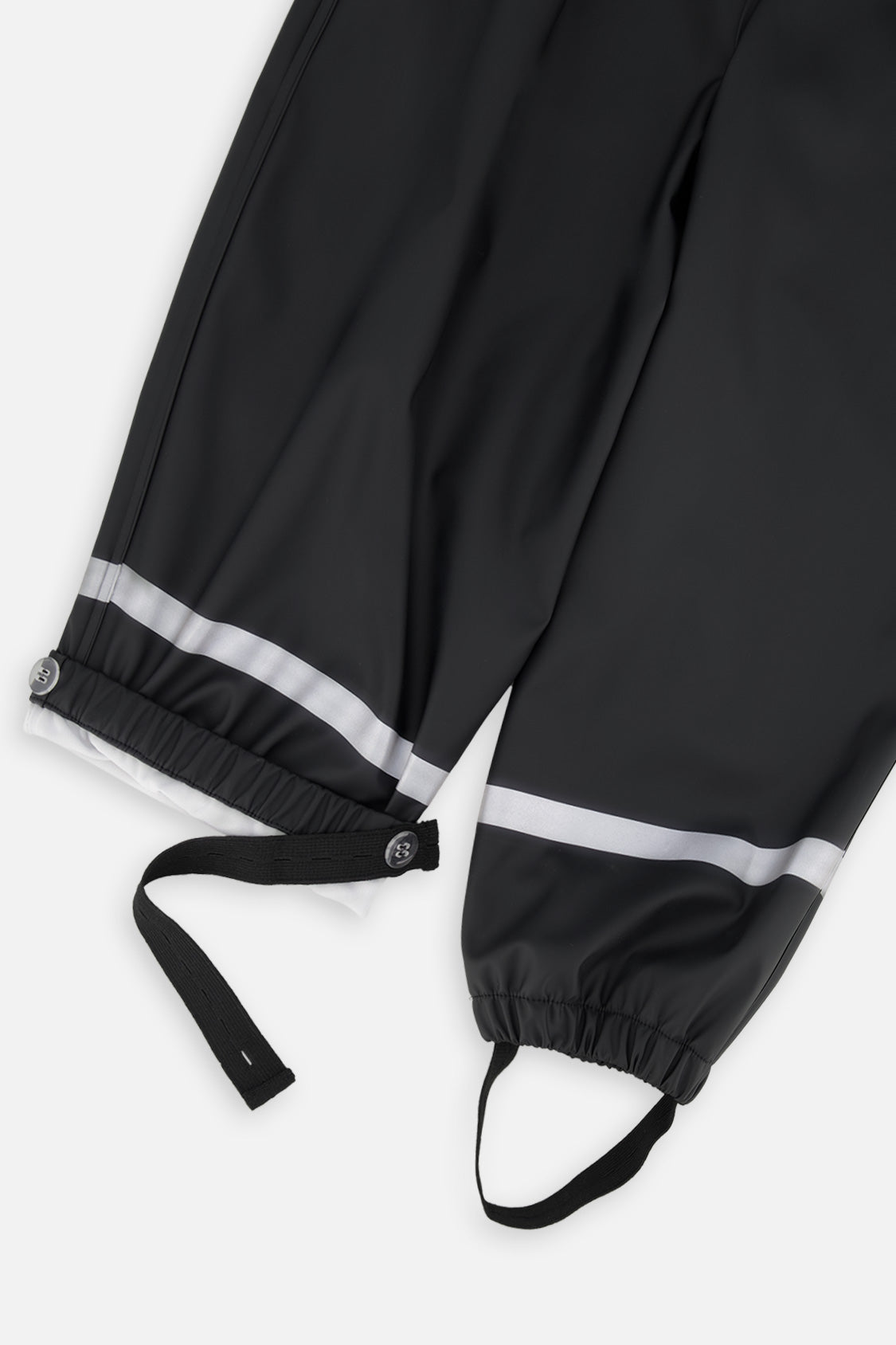 Close-up of the black rain overalls ankles with reflective stripes, snap tabs and foot straps
