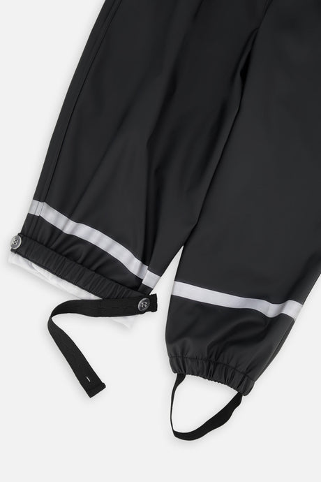 Close-up of the black rain overalls ankles with reflective stripes, snap tabs and foot straps