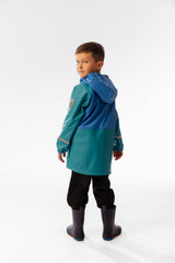 Child wearing the dark turquoise rain jacket in a back three-quarter view with the hood down and navy rain boots