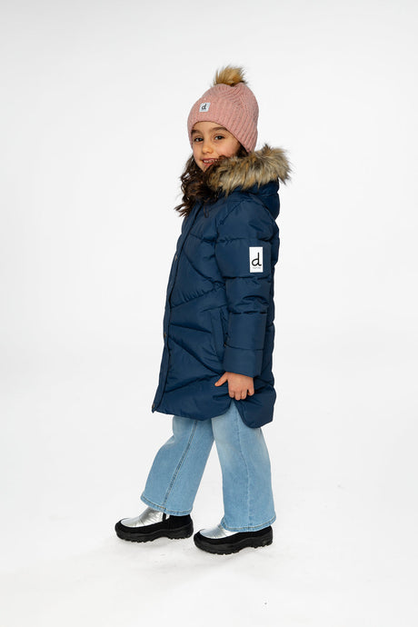 Side view of a child in the long dark blue coat with silver boots and a pink knit hat