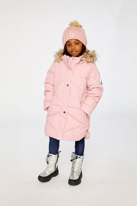 Girl wearing the long pale dusty pink puffer coat with a pink pompom hat and silver boots, front view