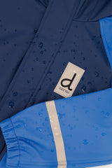 Water beading on the navy chest of the blue rain one-piece beside the logo patch and reflective sleeve band