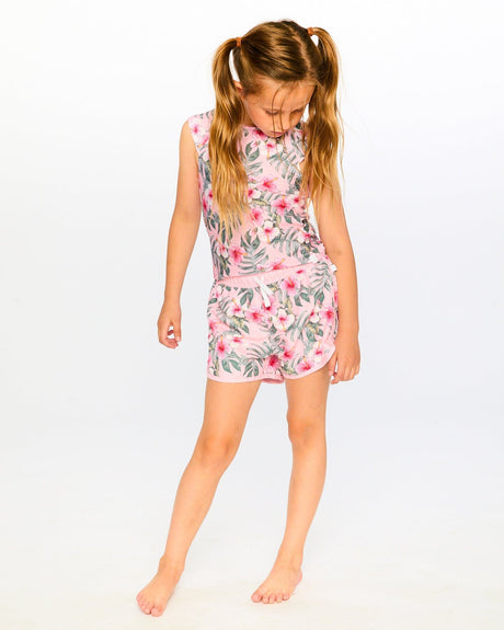 Girl wearing pink hibiscus swim shorts and matching top standing by the water