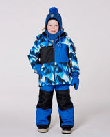 Boy wearing blue jacket and snow pants with detachable hood and snow skirt.