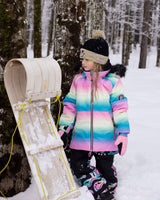 Action shot: girl in rainbow jacket and snow pants, breathable and cozy on the hill.