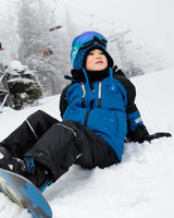 Action shot: boy in blue jacket and snow pants, helmet-friendly hood.