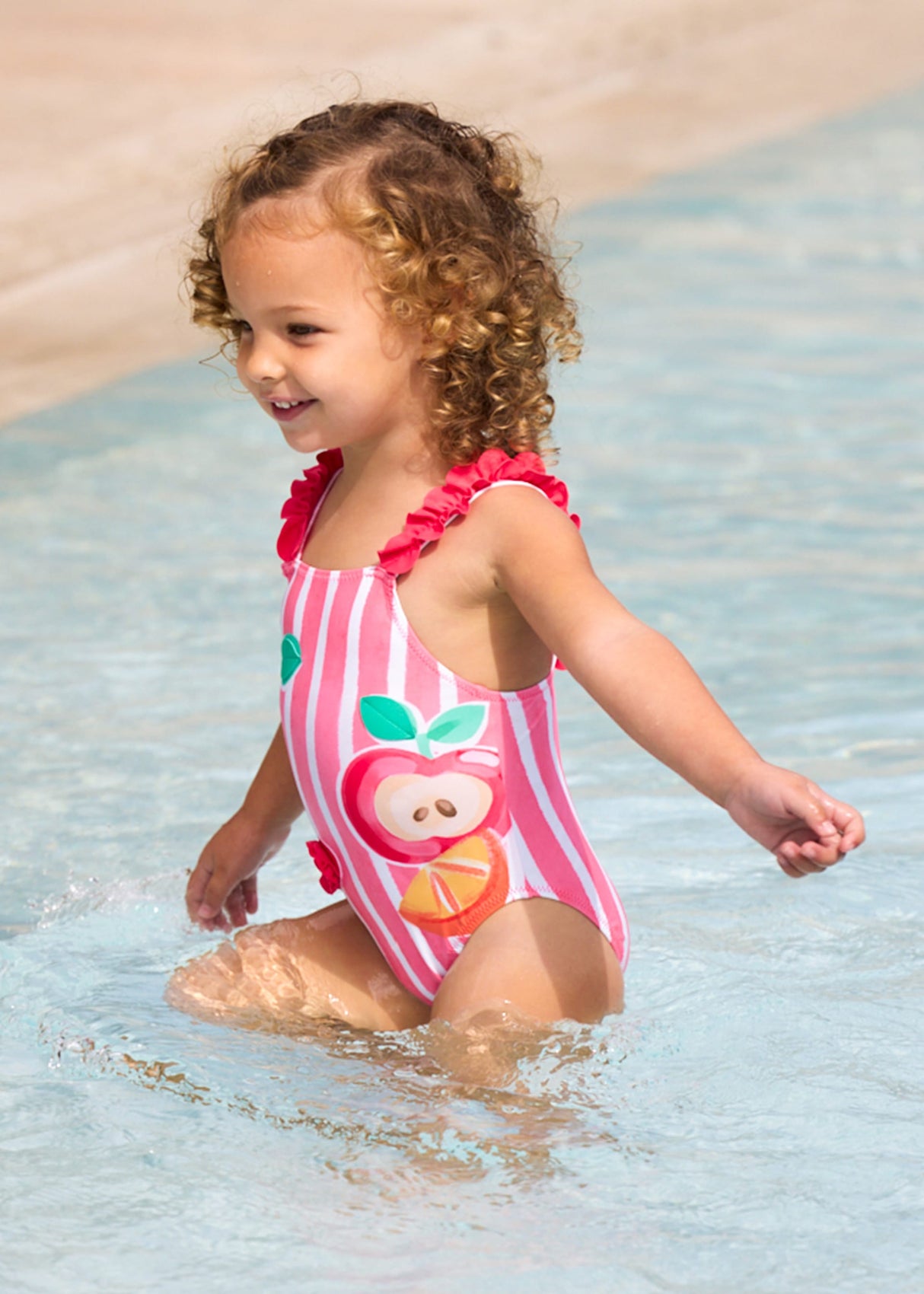 Baby girl wearing Mayoral Pink graphic swimsuit for pool and summer water play.