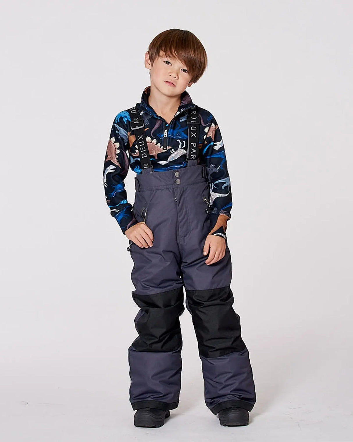 Child in motion wearing dark gray ski bibs side view