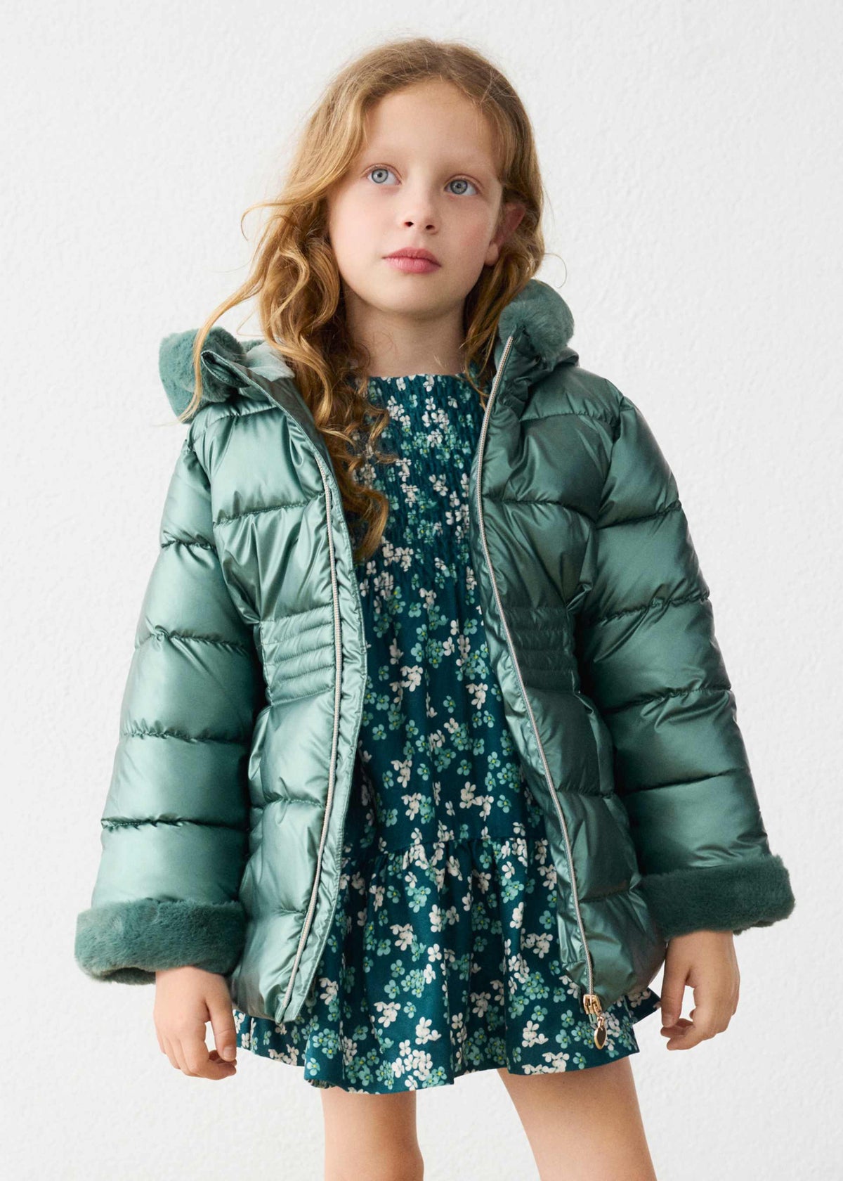 Child wearing the metallic green puffer jacket open over a floral dress