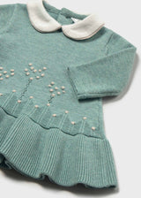 Close-up of the cream collar, dotted flower-stem knit pattern and ribbed ruffle hem on the sage green dress